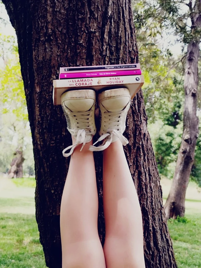 Libros apoyados sobre los tenis, contra un árbol